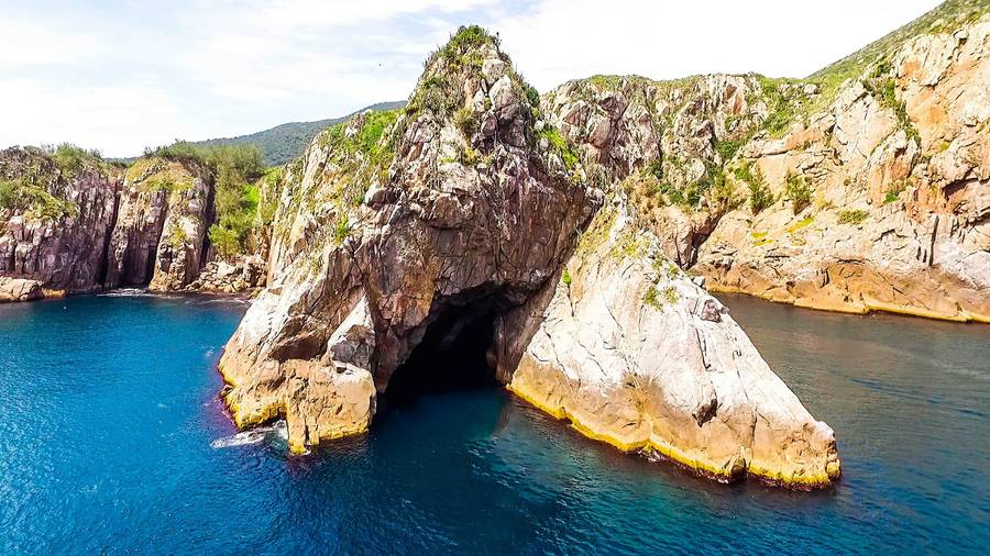 Entrada da Gruta Azul no costão rochoso, com mar azul profundo em volta